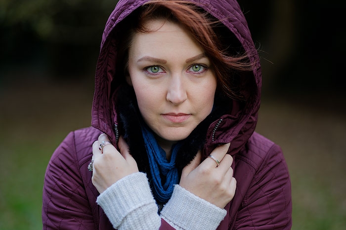 Portrait of a young woman with green eyes & red hair wearing a burgundy hood looking at camera.