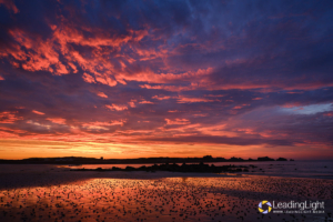 Dramatic clouds glow like fire, reflected in wet sand on Pembroke Bay, Guernsey.