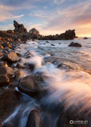 Waves break on the rocky shore of Pulias headland at sunset.